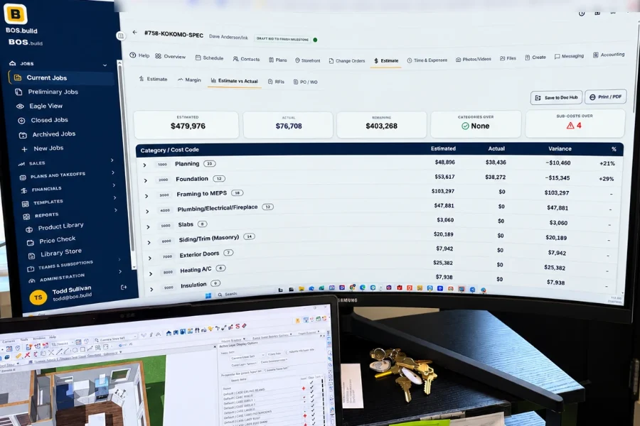 An office desk with BOS open on Estimate vs Actual on a large monitor and a 3D house model on a laptop